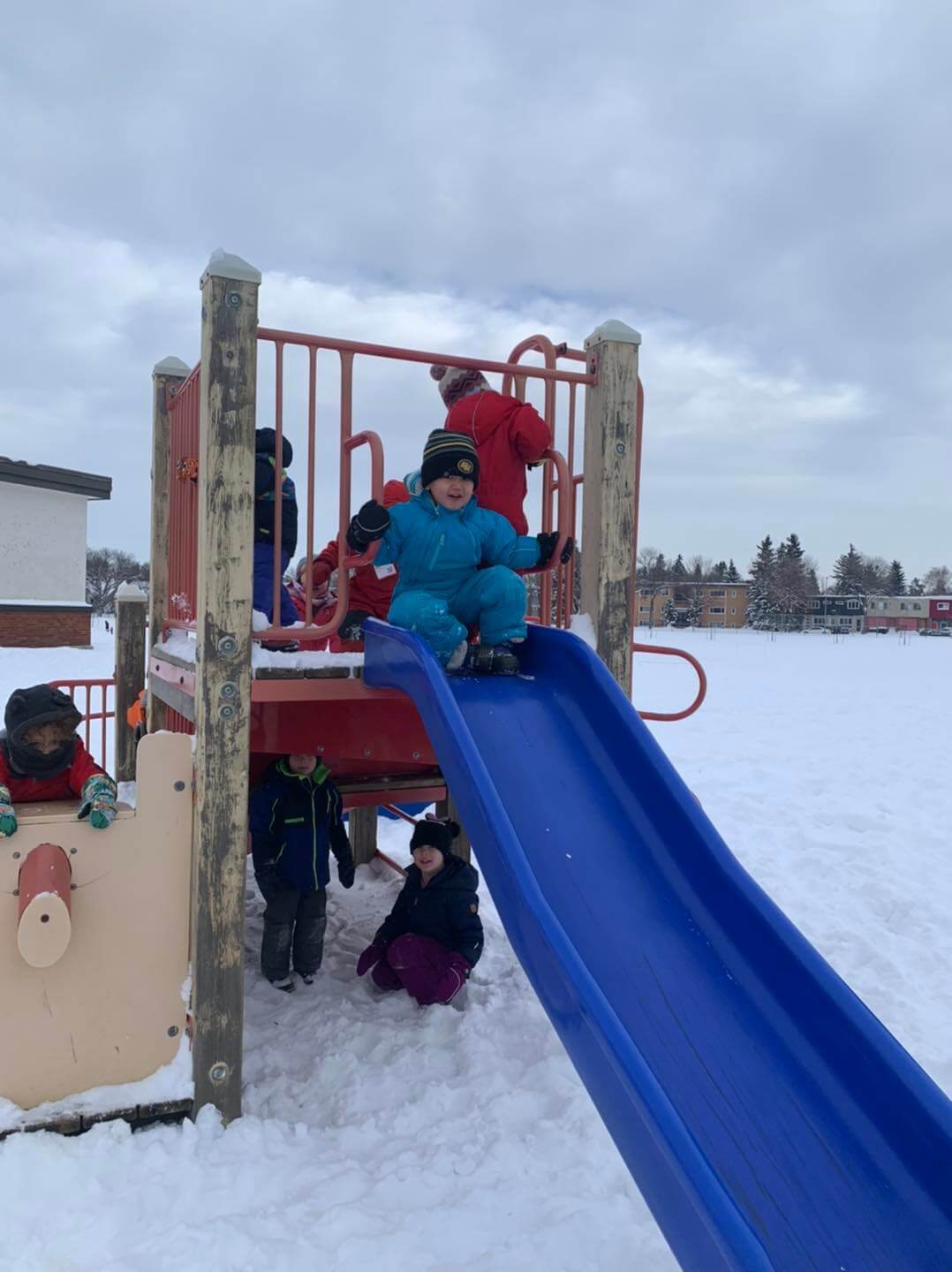 Preschool child in blue winter suit going down the slide at outdoor play at Green Circle Preschool, Edmonton